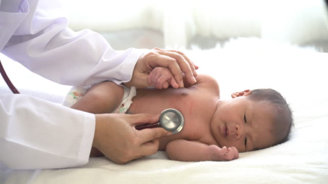 4K-Inyección-media-de-mujeres-pediatras-de-la-mano-sosteniendo-la-mano-de-niña-recién-nacida-asiática-y-usar-estetoscopio-escuchando-a-la-niña-pequeña-latidos-del-corazón-para-el-examen-médico.-Cuidado-de-la-guardería-del-hospital-y-concepto-de-me