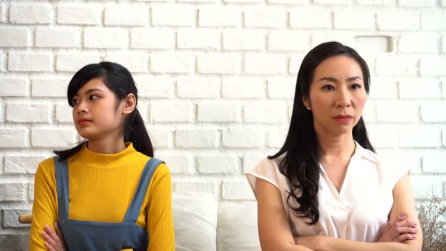 Displeased-Asian-females-sitting-on-sofa