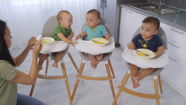 Asiatische-Frau-Fütterung-Kleinkind-Triplets-Püree-zu-Hause