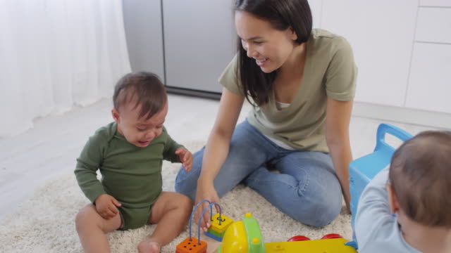 Asiatische-Mutter-trösten-weinen-Kleinkind-und-Geschwister-spielen