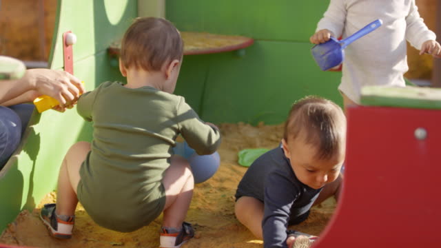 Drei-Kleinkinder-spielen-im-Freien-in-Sandgrube
