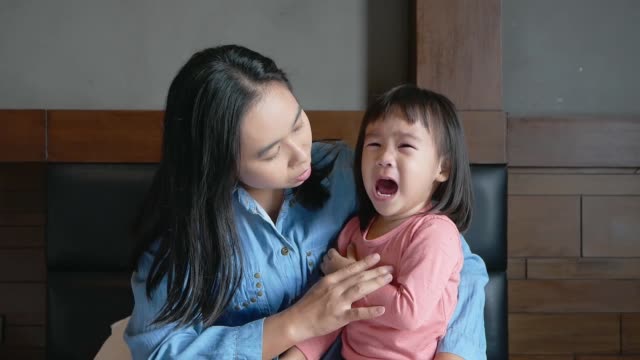 Asian-mother-hugging-her-crying-little-daughter-in-her-arms-and-tries-to-calm-her-on-the-bed.