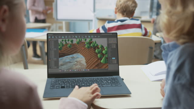 Aula-de-Ciencias-de-la-Computación-de-la-Escuela-Primaria:-Sobre-la-vista-del-hombro-de-dos-niños-que-utilizan-la-computadora-portátil-para-diseñar-el-juego-en-3D,-el-nivel-de-construcción-en-el-videojuego-de-rol-estratégico