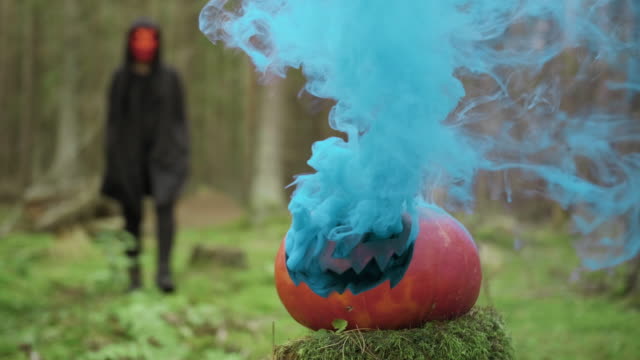 Person-geht-in-Maske-und-Coak-im-Wald-auf-dem-Halloween-mit-rauchigen-Kürbis