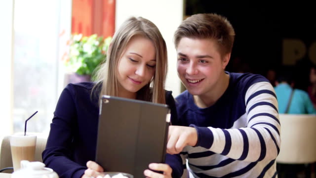 Young-attractive-couple-using-digital-tablet-computer,-looking-at-the-screen-in-cafe.