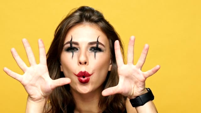 Young-crazy-woman-with-creepy-make-up-scaring-you-and-laughing-isolated-over-yellow-background