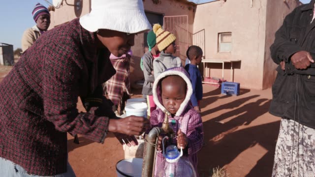 Little-african-girl-collecting-water-from-a-tap-while-woman-and-children-line-up-to-collect-water-in-plastic-containers-due-to-severe-drought-in-South-Africa