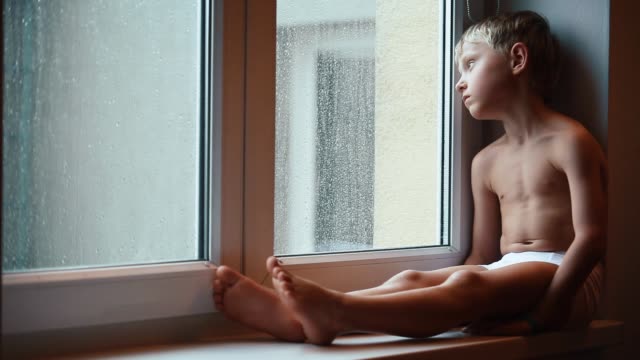 Niño-triste-en-el-alféizar-de-la-ventana-cerca-de-la-ventana