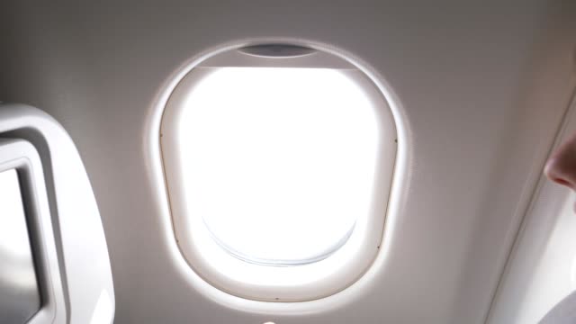 CLOSE-UP:-Woman-traveler-pulls-up-the-blinds-and-looks-through-airplane-window.