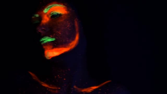 Fashion-sexy-dancer-with-braids-in-neon-light.-Fluorescent-makeup-glowing-under-ultraviolet-light.-Night-club,-party,-halloween-psychedelic-concepts.-Mysterious-woman-with-UV-painting