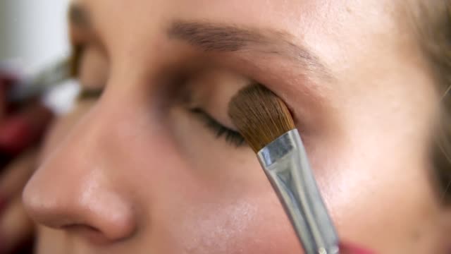 Make-up-artist-applying-light-brown-shadows-on-an-eyelids-with-two-brushes-together,-Close-up-of-a-young-caucasian-woman's-eyes