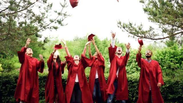 Lenta-de-felices-graduados-lanzan-Birretes-en-el-aire,-riendo-y-celebrando-la-graduación-en-el-campus-de-la-Universidad.-Educación,-el-éxito-y-el-concepto-de-juventud-moderna.