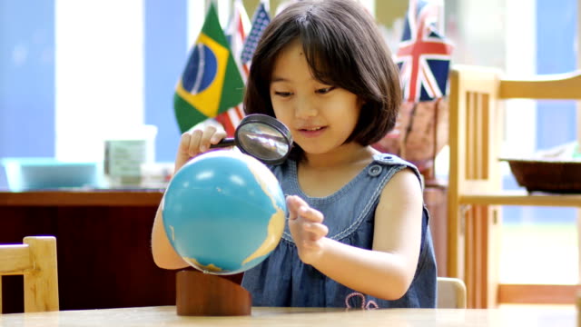 4K-Little-Asian-student-looking-at-globe-with-magnifying-glass