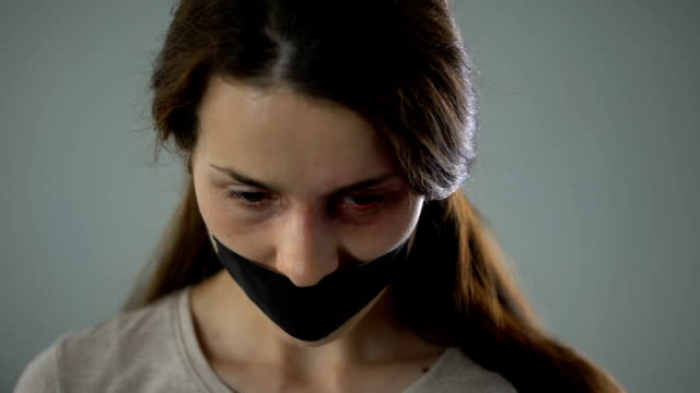 Bruised-woman-with-taped-mouth-sadly-looking-into-camera,-victim-of-abuse