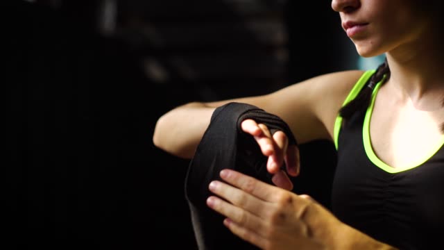 Closeup-panning-fit-woman-wrapping-hands-with-bandage-tape-preparing-for-boxing-training-slow-motion