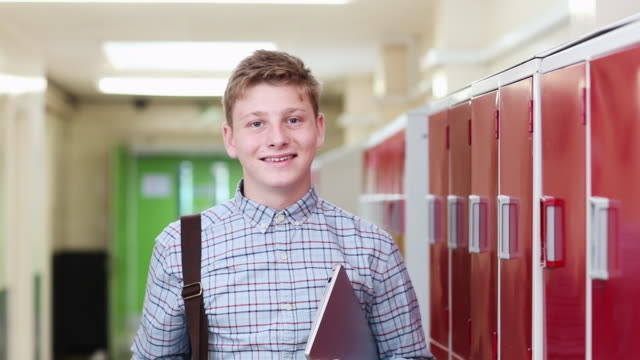 Portrait-Of-Male-High-School-Student-Walking-Down-Corridor-And-Smiling-At-Camera