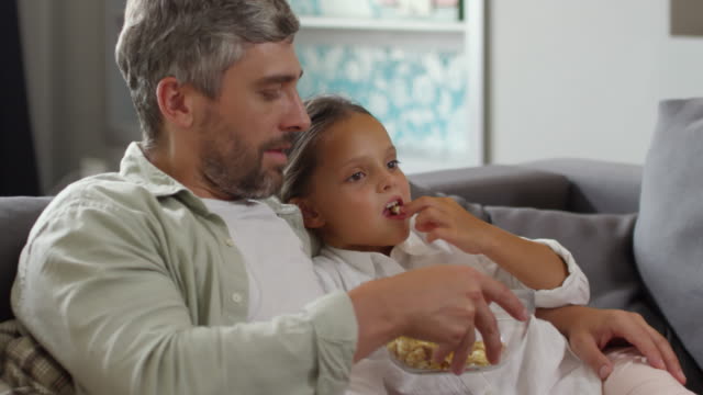 Papa-und-kleines-Mädchen-vor-dem-Fernseher-auf-Sofa-und-essen-Popcorn