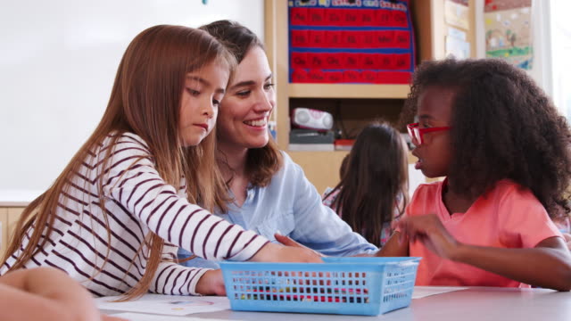 Female-elementary-school-teacher-helping-two-girls-in-class