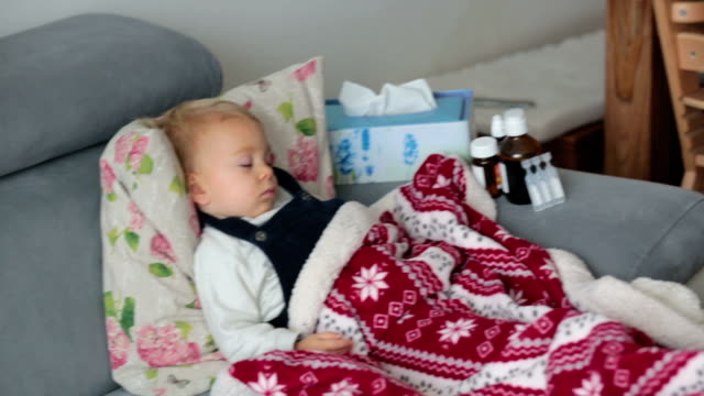 Niño-enfermo,-durmiendo-cubierto-con-una-manta-suave-en-el-sofá-en-la-sala-de-estar,-junto-a-él-la-medicina