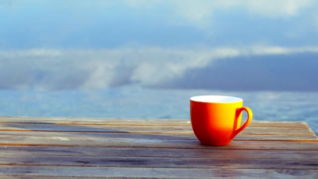 Orange-auf-Tasse-Kaffee-braun-Holztisch-am-Strand-mit-Brandung-des-Meeres-im-Hintergrund.