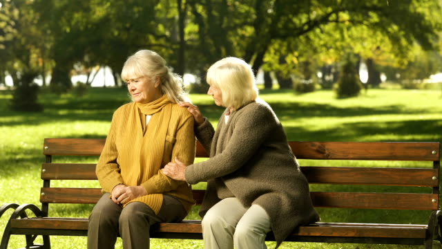 Dama-Senior-reconfortante-viejo-amigo-acerca-de-su-pérdida,-sentado-sobre-un-banco-en-el-Parque