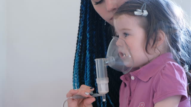 Kleine-süße-Mädchen-mit-ihrer-Mutter-durch-Inhalator-Maske-einatmen.-Verwenden-Sie-Vernebler-und-Inhalator-für-die-Behandlung.