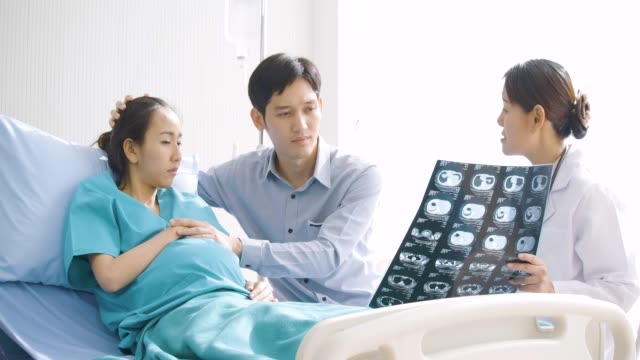 Doctor-showing-X-ray-scan-results-to-pregnant-woman-and-her-husband-with-serious-emotion.-People-with-healthcare-and-medical-concept.