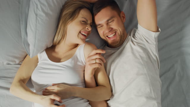 Junges-Liebespaar-Morgen-im-Bett-zu-verbringen,-zeigt-schwangere-junge-Frau-ihrem-Partner-etwas-auf-ein-Touchscreen-Smartphone,-wobei-Selfie-und-Bild-in-sozialen-Netzwerken-teilen.