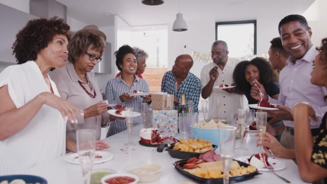 Drei-Generation-schwarzer-Familie-stehen-um-einen-Tisch,-der-Kuchen-isst-und-bei-einer-Familiengeburtstagsfeier
