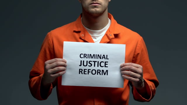Criminal-justice-reform-phrase-on-cardboard-in-hands-of-Caucasian-prisoner