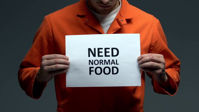Need-normal-food-phrase-on-cardboard-in-hands-of-Caucasian-prisoner,-protest