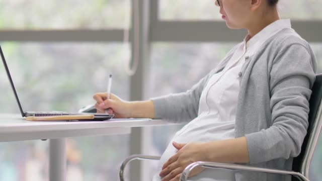 Chinesisch-schwangere-Bürofrau-arbeitet-mit-Laptop-und-Dokumenten