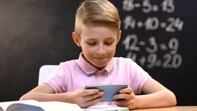 Niño-jugando-videojuego-en-el-teléfono-inteligente-durante-la-lección-de-la-escuela,-mal-alumno