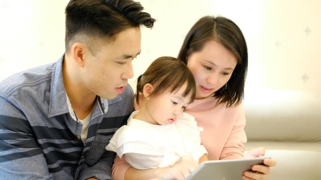 Asiatische-Eltern-Vater-und-Mutter-und-Tochter-spielen-mit-digitalen-Tablet-auf-dem-Sofa