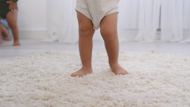 Piernas-de-un-irreconocible-niño-descalzo-aprendiendo-a-caminar-sobre-la-alfombra