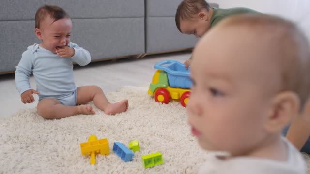 Tres-niños-pequeños-jugando-en-la-alfombra-en-casa-y-la-madre-mirando