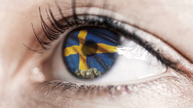 mujer-ojo-verde-en-primer-plano-con-la-bandera-de-Suecia-en-el-iris-con-el-movimiento-del-viento.-concepto-de-vídeo