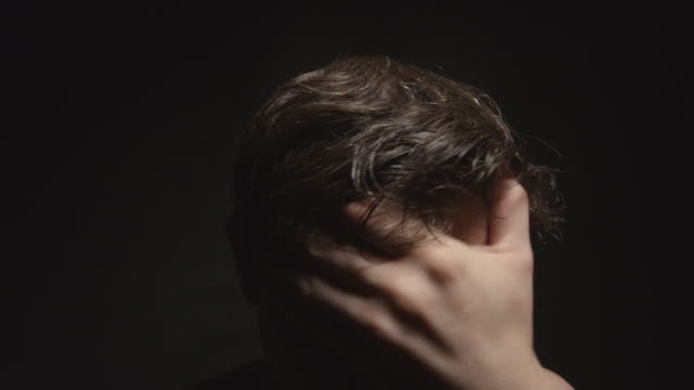Worried-man-touches-his-wet-hair-by-hand-in-dark-room