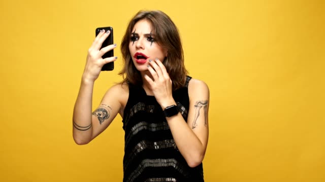 Verärgert-Dame-mit-Halloween-make-up-mit-Smartphone-und-verärgert-über-ihr-Aussehen-über-gelb-isoliert