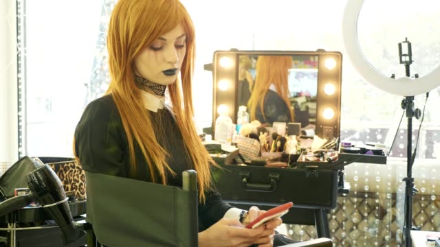 Junge-schöne-Mädchen-mit-Halloween-Make-up-mit-Smartphone-im-Schönheitssalon