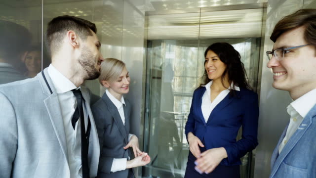 Tiro-de-seguimiento-de-mujeres-empresarias-y-empresarios-colegas-hablando-en-el-movimiento-del-elevador-y-salen-de-él-y-caminar-en-el-hall-de-moderno-centro-de-negocios