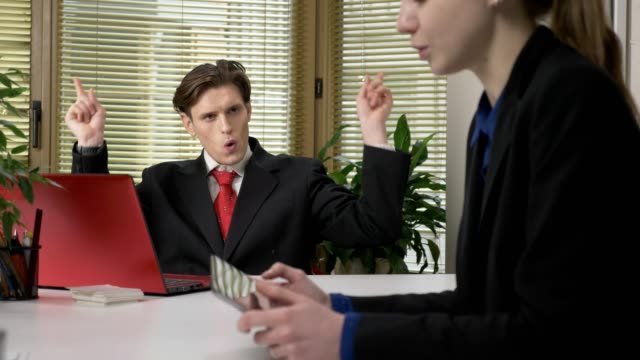 A-young-guy-in-a-suit-shows-a-heart-sign-to-a-female-employee.-Sign-of-love,-flirting,-work-in-the-office-concept.-60-fps
