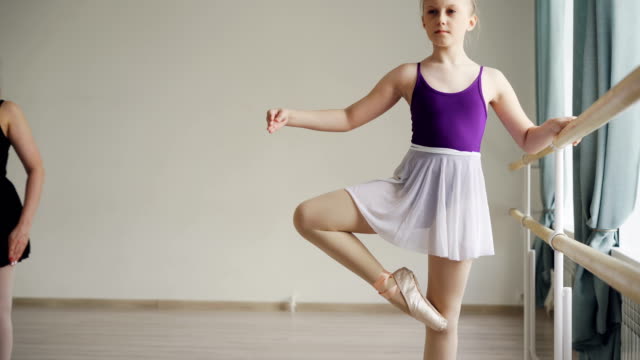 Chica-bonita-en-mono-y-tutu-es-tener-práctica-de-ballet-individual-aprender-movimientos-y-posiciones-con-profesional-docente-en-la-escuela-de-ballet.