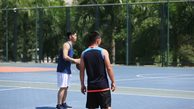 adultos-jóvenes-asiáticos-jugando-baloncesto-en-la-cancha-al-aire-libre