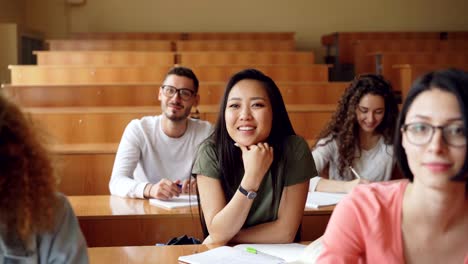 Hübsche-Asiatin-ist-Hand-heben-und-Frage-während-der-Vorlesung-an-der-Hochschule,-ihren-Mitschülern-sitzen-am-Schreibtisch-Lächeln-und-lachen.-Bildung-und-Jugend-Konzept.