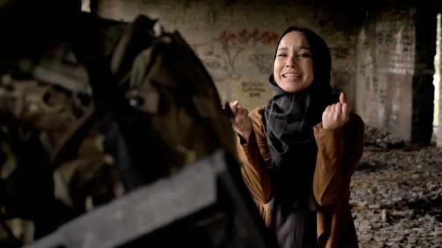 Young-muslim-woman-in-hijab-screaming-and-crying-behind-soldier-with-ammunition-and-weapon,-standing-in-abandoned-building,-war-concept