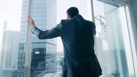 Following-Shot-of-the-Confident-Businessman-in-a-Suit-Walking-Through-His-Office-and-Looking-out-of-the-Window-Thoughtfully.-Stylish-Modern-Business-Office-with-Personal-Computer-and-Big-City-View.