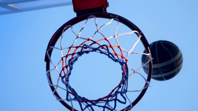 Basketball-bumping-into-hoop-and-passing-through-ring,-outdoor-gym-with-blue-sky-above