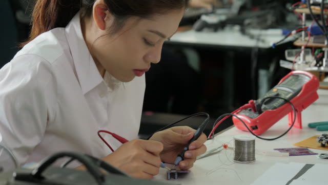 Ingeniero-en-electrónica-mujer-mide-la-señal-en-el-circuito-eléctrico-en-su-taller.-Estudiante-chica-estudiando-electrónica-en-aula.