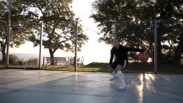 Side-footage-of-a-young-girl-basketball-player-training-and-exercising-outdoors-on-the-local-court.-Dribbling-with-the-ball,-bouncing-and-make-a-shot